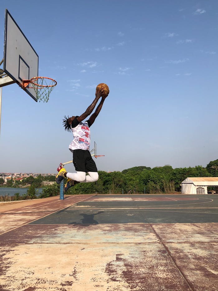 services-01 Athlete performing a powerful dunk on an outdoor basketball court under a clear blue sky.