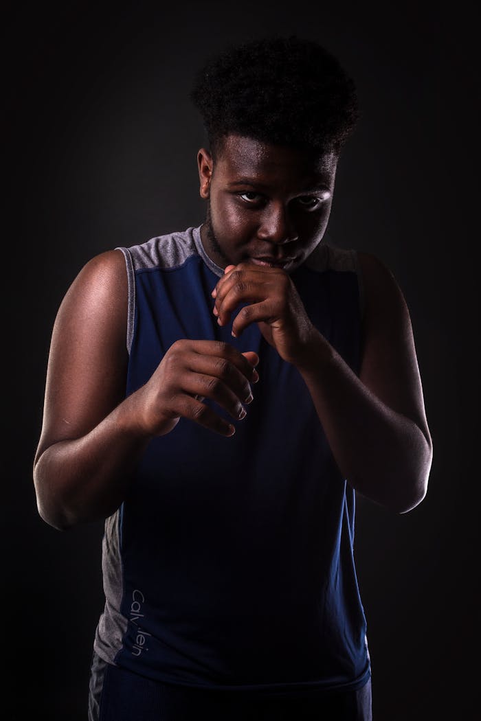 services-02 A young African American boxer poses confidently in a dark studio setting, ready for action.