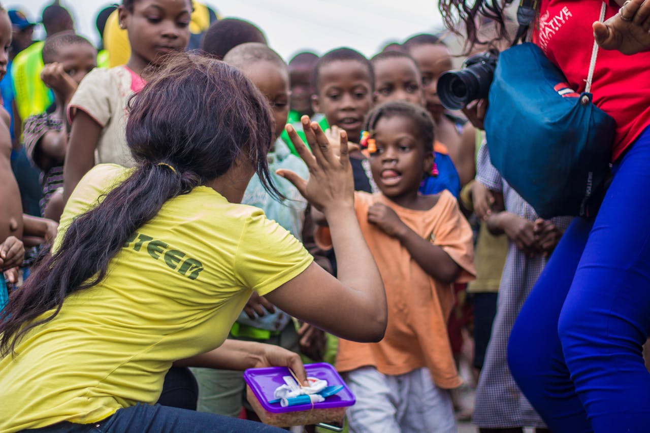 services-04 A woman engages with children through a high-five in a vibrant community setting.